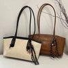 A beige leather tote bag with black leather handles and strap details is displayed next to a brown leather tote bag.