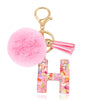 A gold-colored keychain featuring a fluffy pink pom-pom and a resin letter H charm.