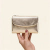 A hand holds a gold metallic leather mini card holder wallet.