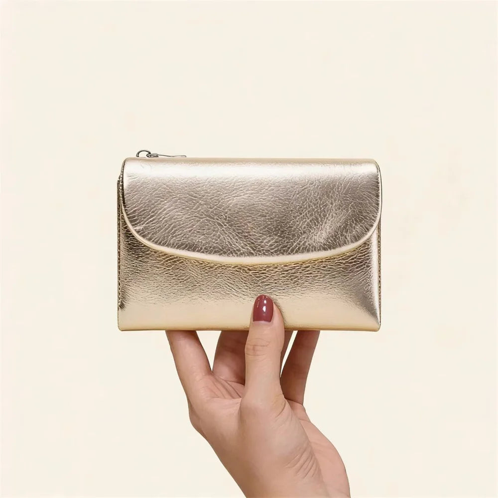 A hand holds a gold metallic leather mini card holder wallet.