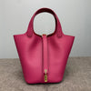 A magenta leather bucket bag with a gold-toned closure and strap, shown from the front.