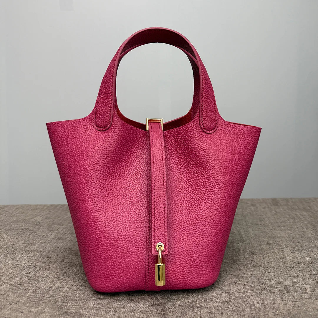 A magenta leather bucket bag with a gold-toned closure and strap, shown from the front.