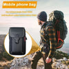 A man wearing a plaid shirt is carrying a black mobile phone bag on his backpack outdoors.