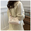A woman holds a light pink embroidered crossbody shoulder bag against a white background.