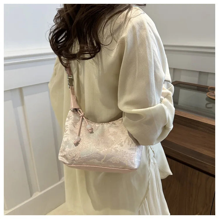 A woman holds a light pink embroidered crossbody shoulder bag against a white background.