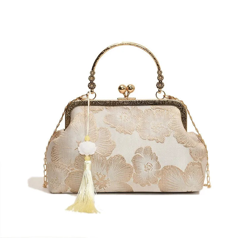 A beige embroidered silk evening clutch with a gold chain strap and tassel detail.