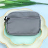 A gray nylon mini coin purse with a double zipper is placed on a light green plate.