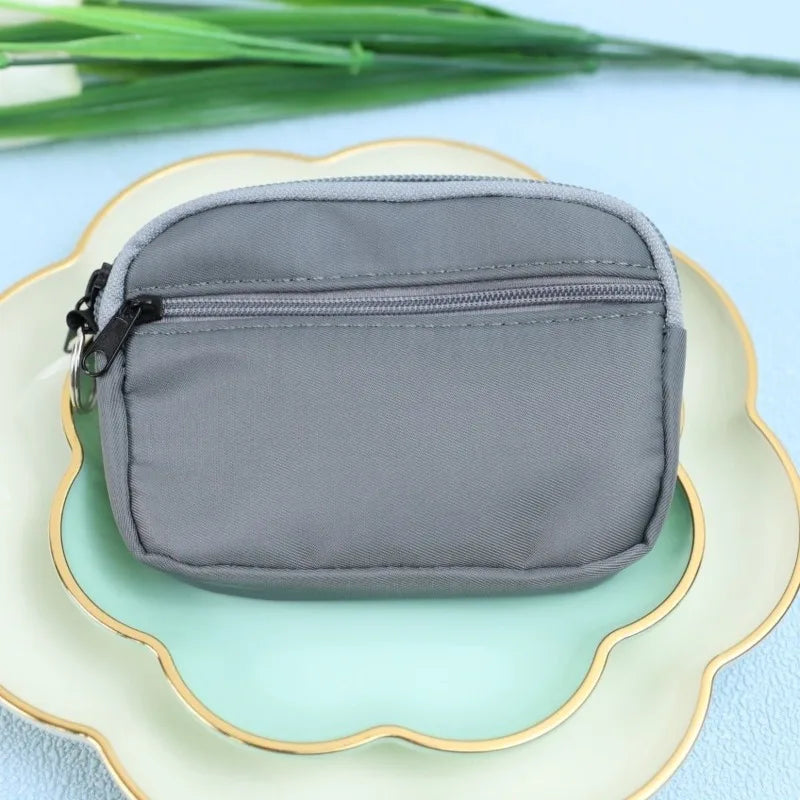 A gray nylon mini coin purse with a double zipper is placed on a light green plate.