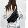 A person is shown from the back wearing a black plaid crossbody chest bag with an adjustable strap over a white t-shirt.