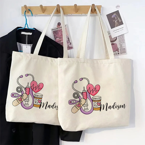 A cream canvas tote bag featuring a pink stethoscope and heart design with the name Madison printed on it.