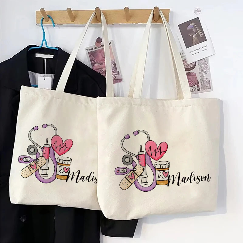 A cream canvas tote bag featuring a pink stethoscope and heart design with the name Madison printed on it.