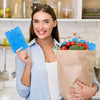 Eine Frau hält ein blaues wiederverwendbares Kühlpack und eine braune Papiertüte mit frischen roten Tomaten und grünen Gemüse