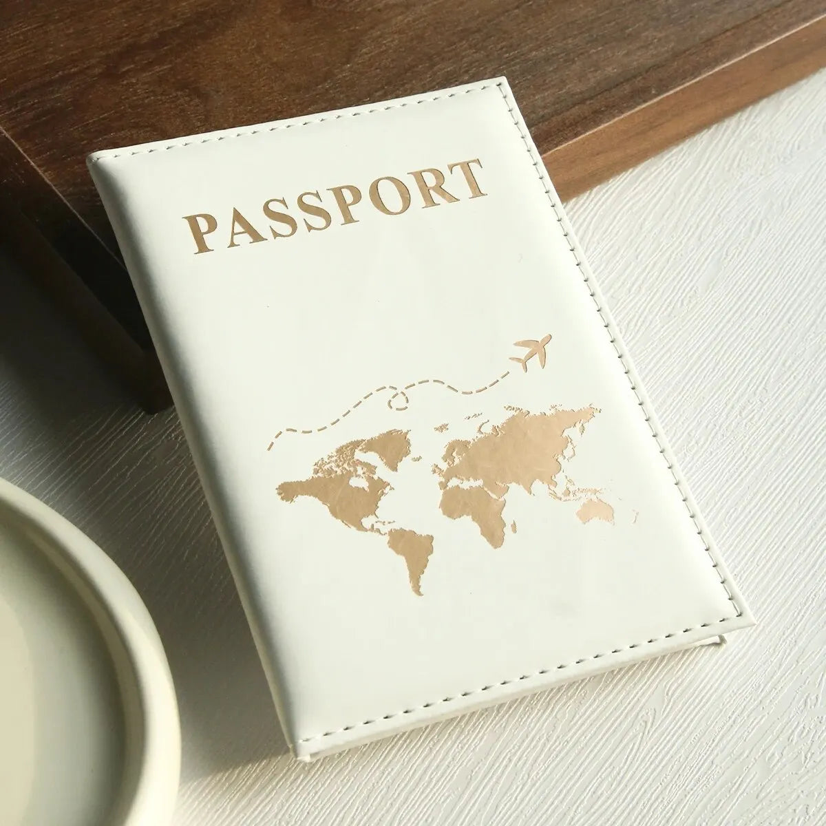 Cremfarbener Leder-Reisepasshülle mit goldfarbiger Folierung einer Weltkarte und dem Wort PASSPORT.