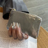 A silver-toned leather compact coin purse and key holder is shown held by a person's fingers.