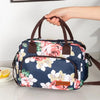 Una bolsa de almuerzo floral azul marino con asas marrones siendo sostenida por una mano.