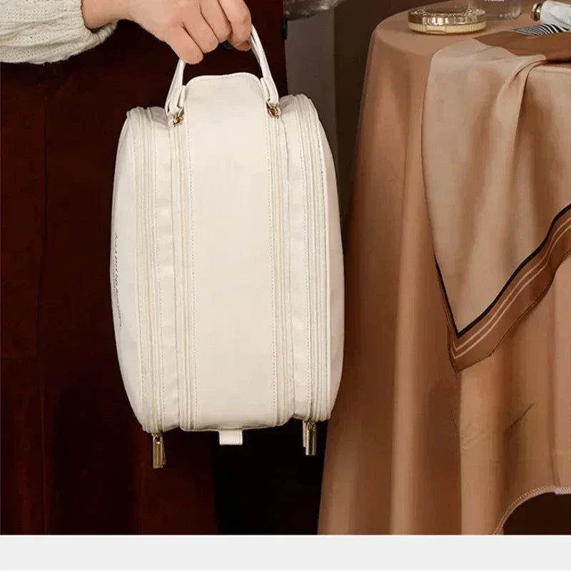 A cream-colored PU leather travel makeup organizer with double zippers is being held by a hand, set against a brown tableclot