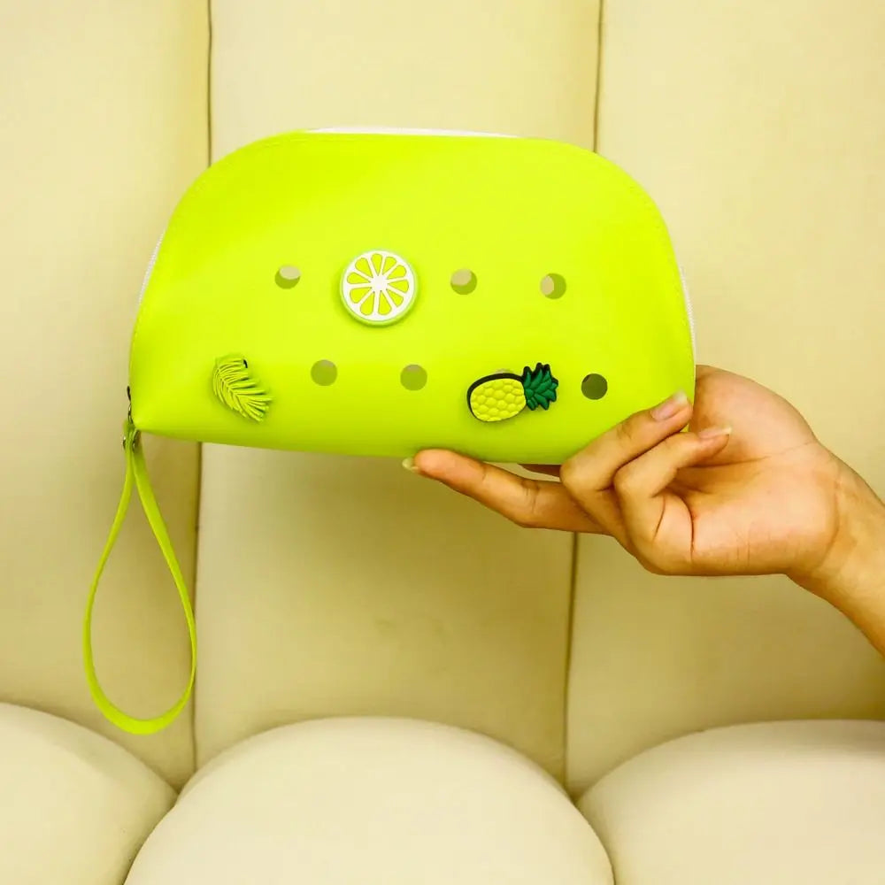 A hand holds a bright lime green silicone coin pouch with drainage holes against a light background.