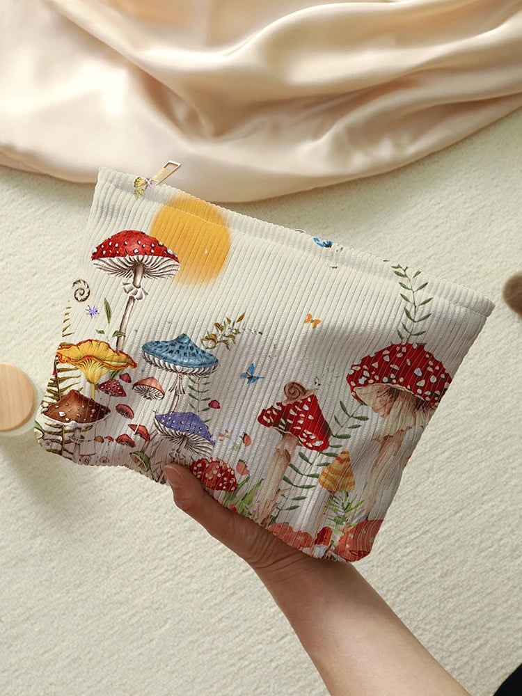 A beige makeup bag featuring a fairytale mushroom and butterfly print, held by a hand against a light background.