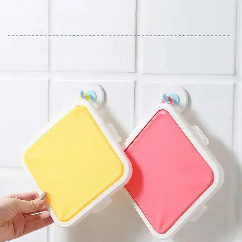 A hand holds a pink silicone reusable sandwich and lunch container against a white tiled background.