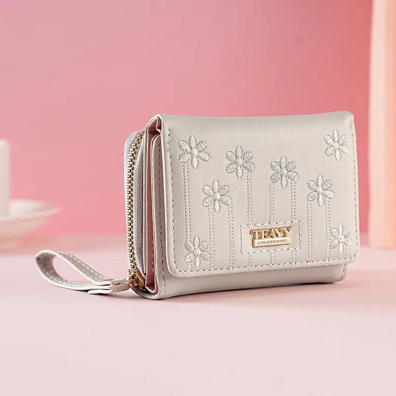 A light beige compact PU leather women's wallet with a zipper closure and floral embroidery on the front.