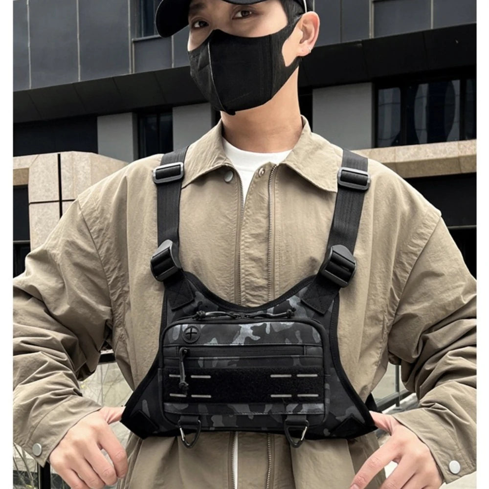 Un jeune homme portant une veste beige et un masque noir tient un sac de sport noir multi-usage.