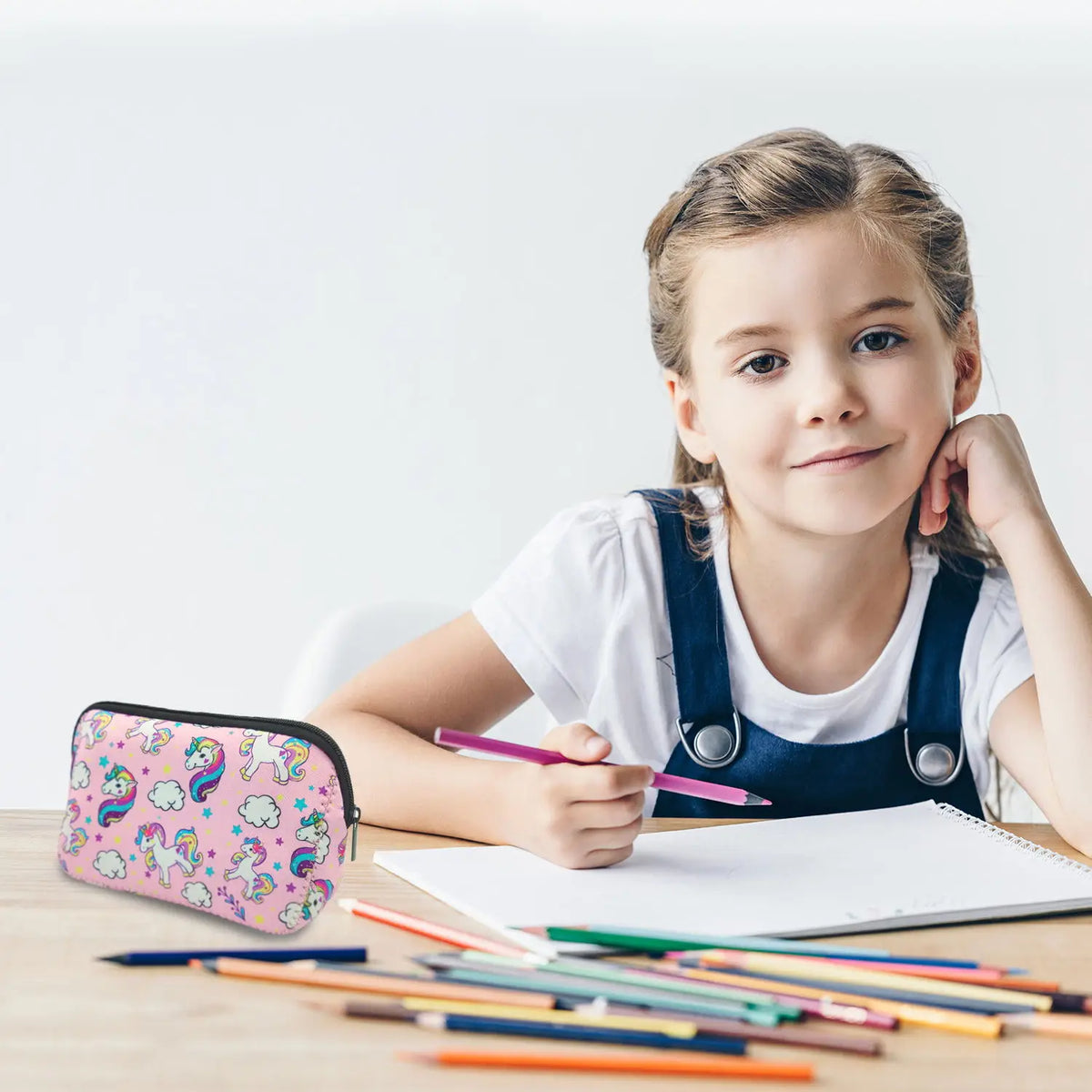 A young girl holds a pink and purple portable neoprene cosmetic organizer bag while writing on a notebook.