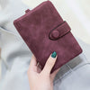 A close-up of a deep plum card wallet with a stitched detail, held by a hand against a light gray fabric.