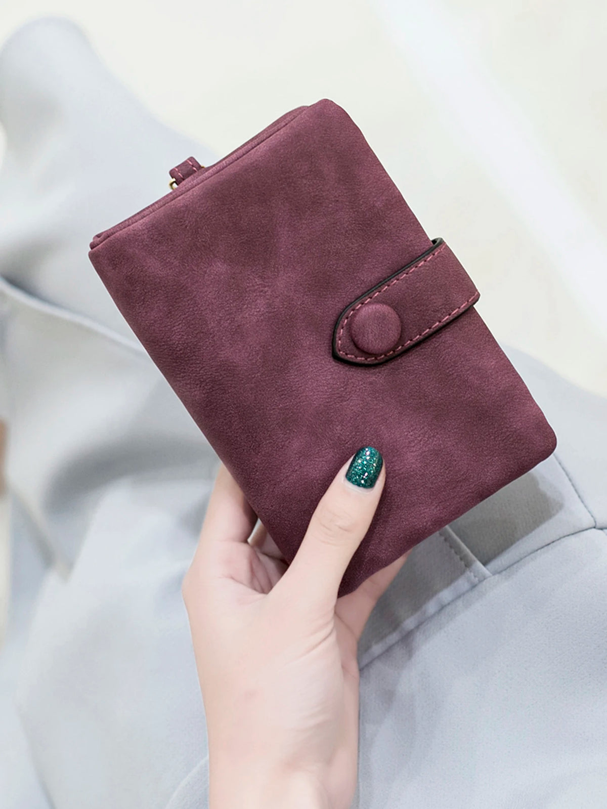 A close-up of a deep plum card wallet with a stitched detail, held by a hand against a light gray fabric.