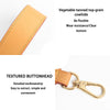 A close-up of a vegetable-tanned top-grain cowhide leather strap with a textured buttonhead and brass hardware.