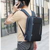A person wearing a beige shirt and gray pants is using a phone while carrying a dark blue nylon travel backpack.