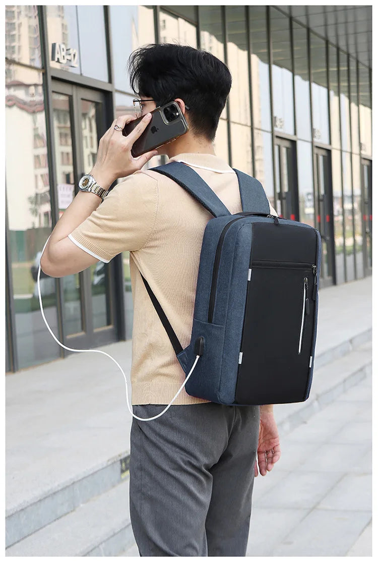 A person wearing a beige shirt and gray pants is using a phone while carrying a dark blue nylon travel backpack.