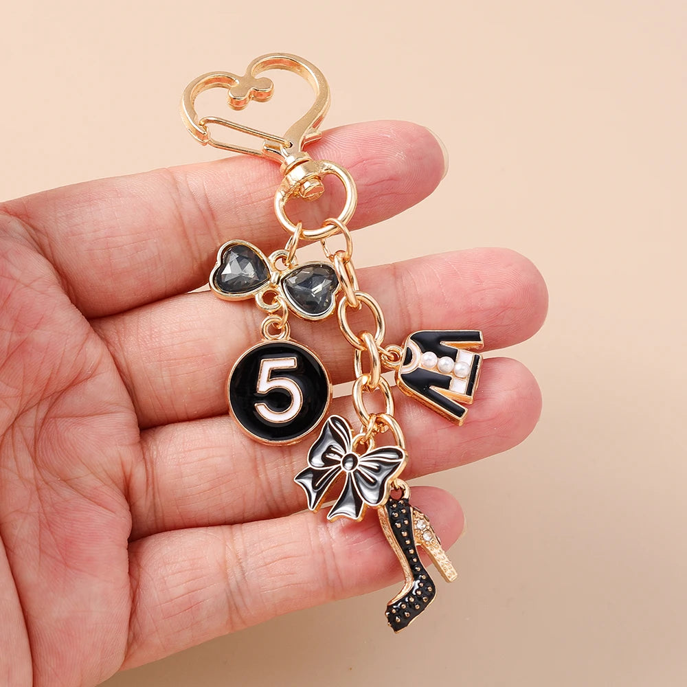 A gold-toned enamel heart keychain featuring a five-pointed number and a bow design, held in a hand.