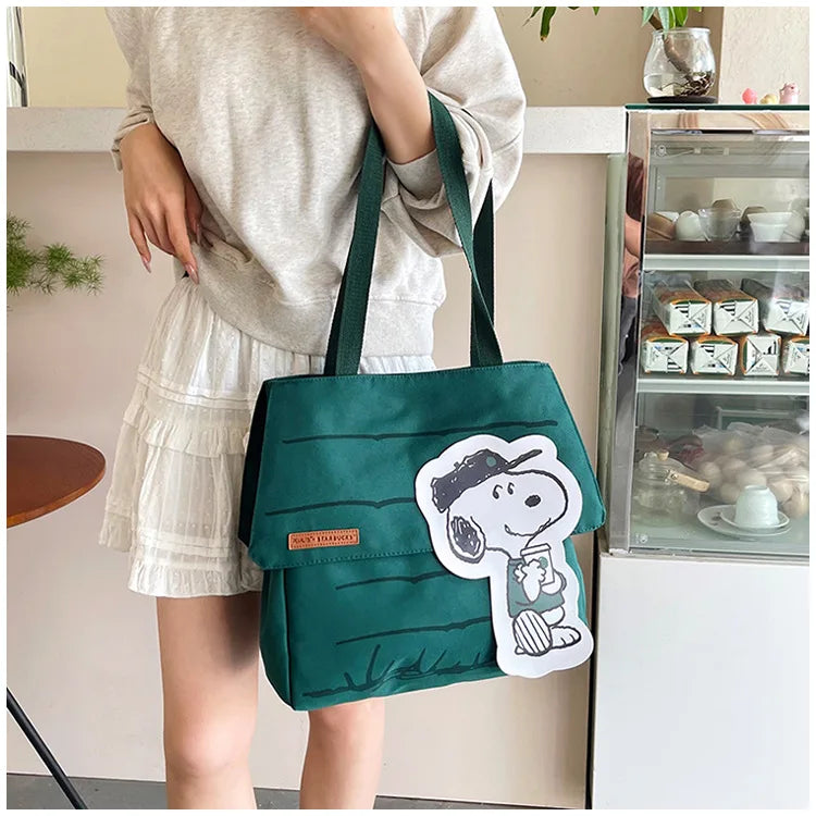 A woman holds a dark green Snoopy canvas tote bag with a white Snoopy graphic.