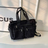 A black textured corduroy tote bag with adjustable straps resting on a white surface.