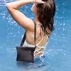 A woman with wet hair is holding her hand above her head in a blue water environment, wearing a white top and a black waterpr