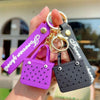 A hand holds a silicone heart beach bag keychain with a black and purple design.