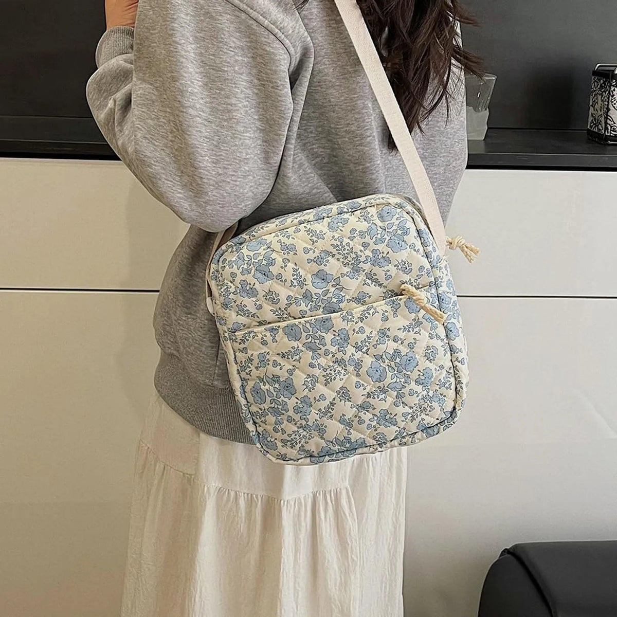 A light blue floral quilted backpack set worn by a person, paired with a gray sweater and white skirt.