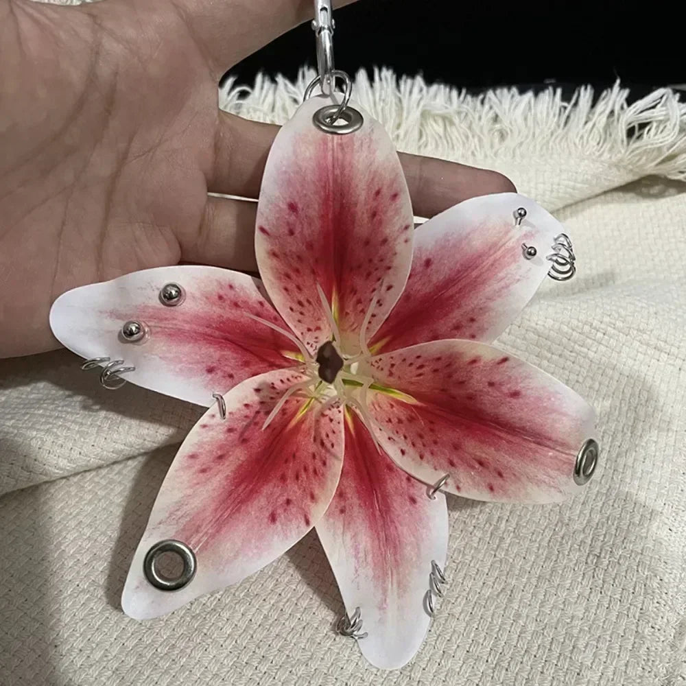 A realistic pink and white orchid flower keychain is held in a hand against a light background.