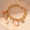 Gold chain bracelet featuring ocean pearl charms including a starfish, shell, and diamond accents on a natural stone backgrou