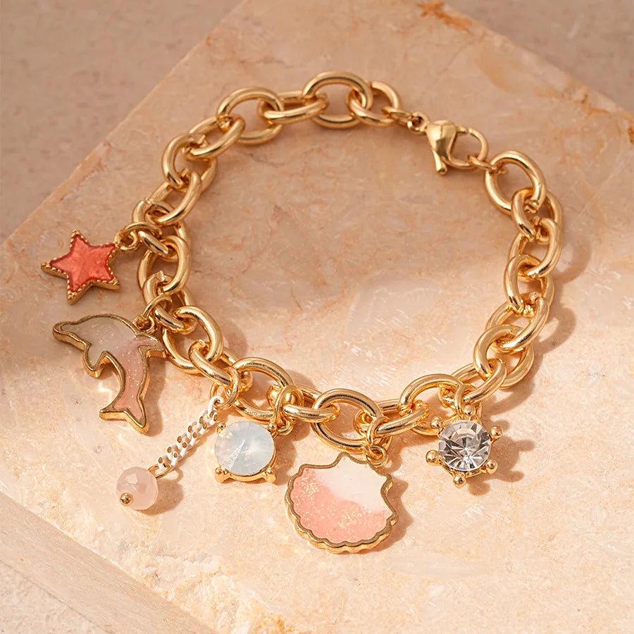 Gold chain bracelet featuring ocean pearl charms including a starfish, shell, and diamond accents on a natural stone backgrou
