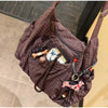 A dark purple plaid nylon drawstring tote bag filled with various small accessories and leather goods.