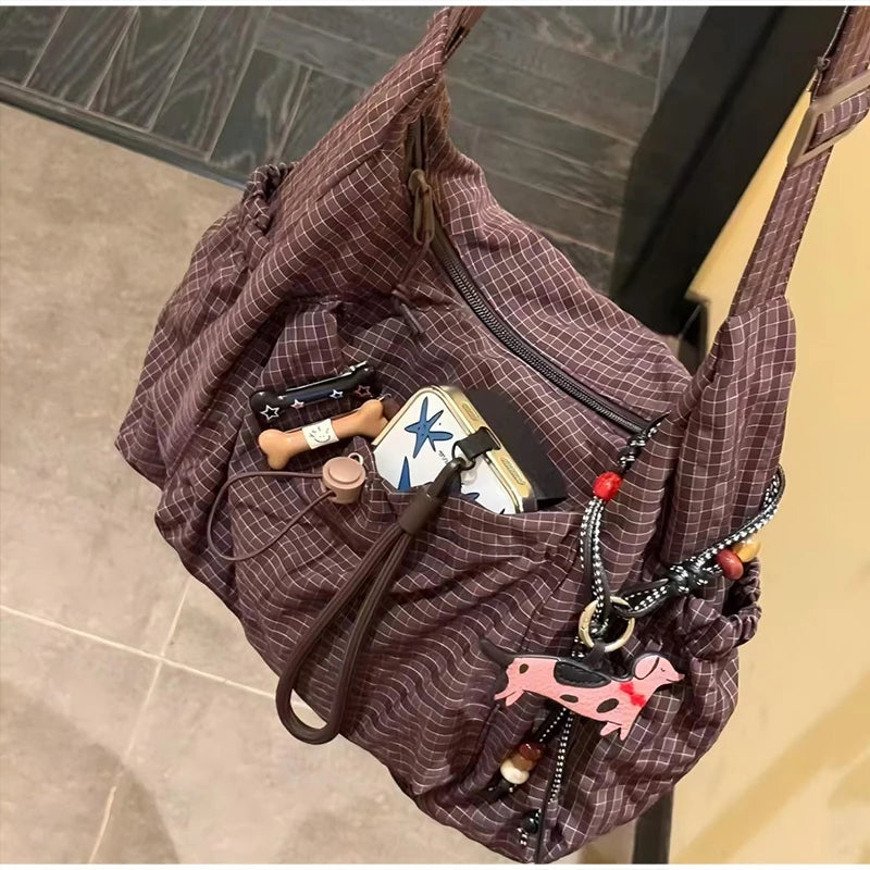 A dark purple plaid nylon drawstring tote bag filled with various small accessories and leather goods.