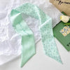 Foulard de cheveux floral vert menthe soie drapé sur du papier blanc à côté d'une boîte verte.