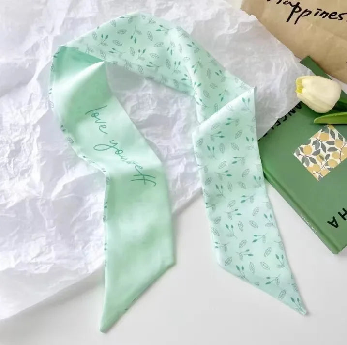 Foulard de cheveux floral vert menthe soie drapé sur du papier blanc à côté d'une boîte verte.