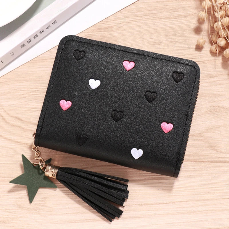 Black compact PU leather wallet with a zipper closure decorated with small pink and white heart embellishments and a black ta