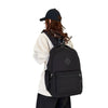 A person wearing a black baseball cap and a beige top is carrying a black durable nylon commuter backpack.