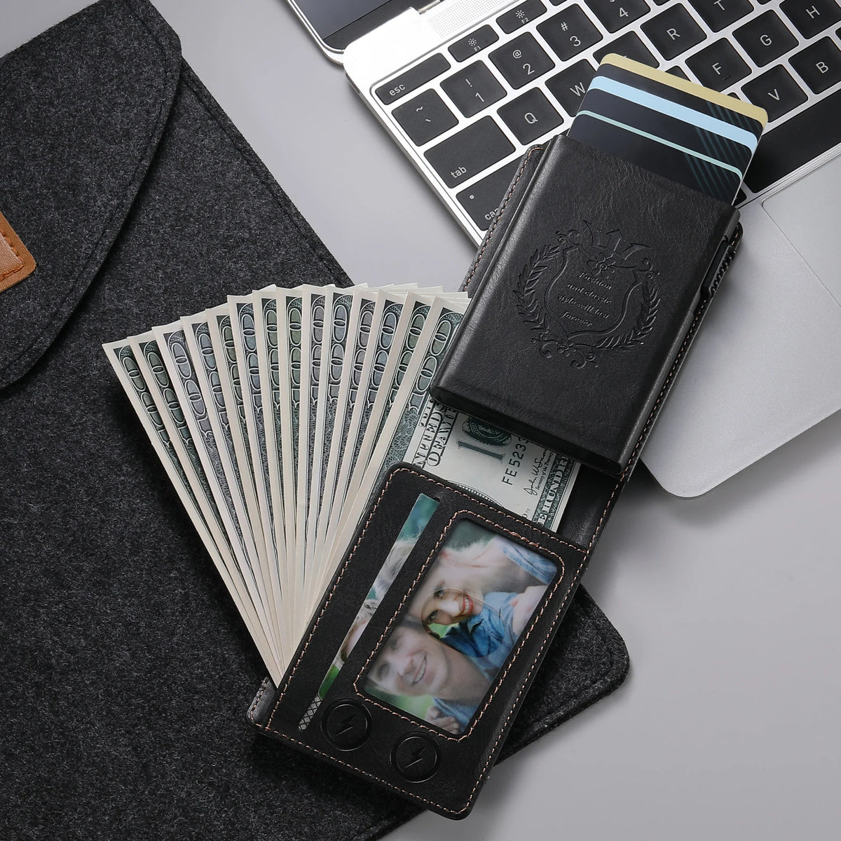 A black anti-RFID blocking PU leather card holder is shown next to a laptop and a stack of US dollar bills.