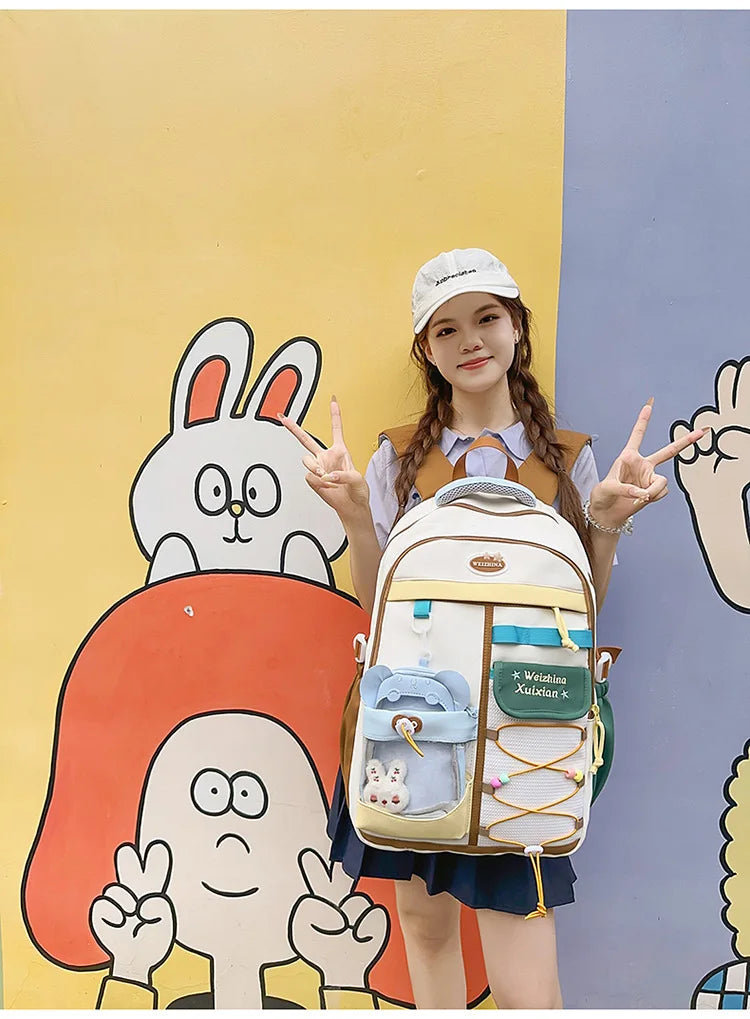 A young woman wearing a white cap and a beige backpack stands in front of colorful wall art featuring cartoon rabbits and fig