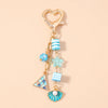 Gold-toned starfish keychain featuring blue and white striped beads, a star charm, and a pearl accent.