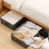 A woman is placing folded baby clothes into a foldable under-bed storage box with a clear window.